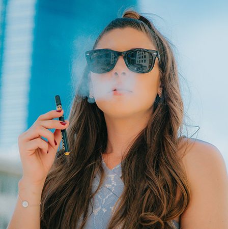 woman with long wavy brown hair and black sunglasses vaping