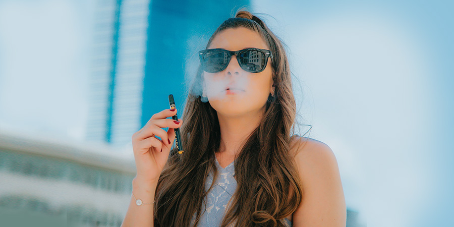 woman with long wavy brown hair and black sunglasses vaping