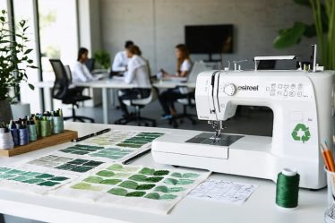 Diverse team of fashion professionals working on sustainable designs, featuring organic fabric swatches and eco-friendly fashion sketches in a modern studio.