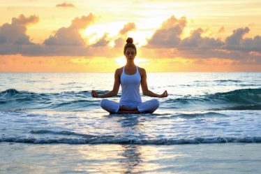 Person practicing yoga on a beach at sunrise, embodying the transition from stress to harmony and peace through mindfulness and self-care.