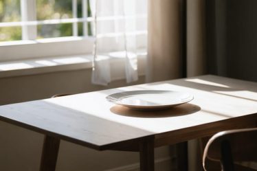 A serene dining table setup with natural light, featuring a minimalistic table arrangement and a single place setting to encourage mindful eating.