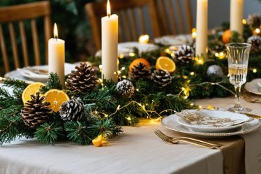 A festive holiday table featuring eco-friendly decorations, including pinecone centerpieces, dried orange garlands, and natural greenery, illuminated by warm LED lights.