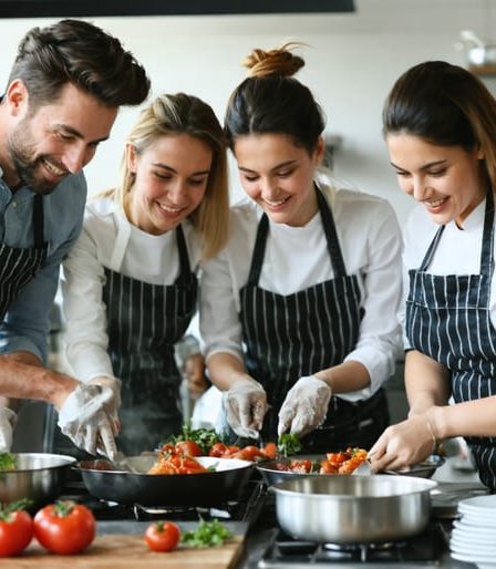 A diverse team of corporate professionals enjoying a hands-on cooking class, collaborating and smiling while preparing dishes in a professional kitchen setting.