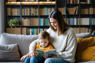 Parent and child sitting together on a couch, surrounded by books, demonstrating a moment of connection and reflection on parenting beliefs.