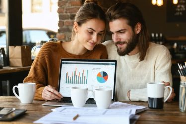 A couple in a cozy coffee shop, discussing their finances with a laptop and documents, embodying collaboration and financial harmony.