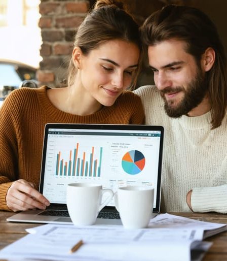 A couple in a cozy coffee shop, discussing their finances with a laptop and documents, embodying collaboration and financial harmony.