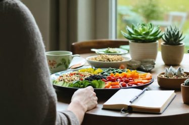 A person peacefully examining their balanced meal with colorful vegetables and grains, accompanied by mindful elements like a journal and a cup of herbal tea, illustrating the concept of mindful eating in a serene dining environment.