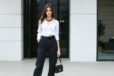 Petite woman standing confidently in a high-waisted, monochromatic outfit with vertical stripes, demonstrating styling tricks for elongating her frame.