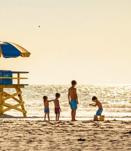 Calm beach setting with a lifeguard tower, where a family enjoys building sandcastles and playing in shallow, gentle waters while parents relax under an umbrella.