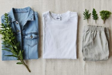 Flat lay of sustainable fashion essentials, including an organic cotton t-shirt, a hemp denim jacket, and linen trousers, on a textured neutral background with eco-friendly elements.