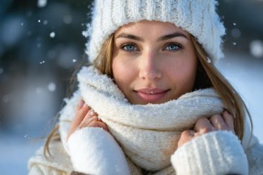 Women with healthy skin standing between a winter landscape and a cozy indoor setting, symbolizing the balance of protective skincare routines against harsh winter elements.