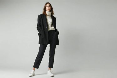 "A conceptual illustration of a woman embodying Ellen DeGeneres' iconic winter style: a blazer and sweater combination paired with tailored pants and sneakers, set against a winter city backdrop."