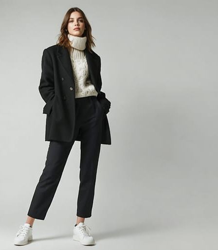 "A conceptual illustration of a woman embodying Ellen DeGeneres' iconic winter style: a blazer and sweater combination paired with tailored pants and sneakers, set against a winter city backdrop."
