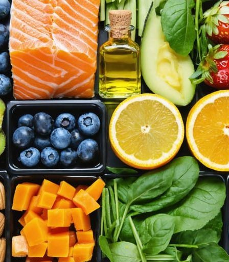 Colorful collage of skin-benefiting foods including salmon, berries, leafy greens, citrus fruits, nuts, seeds, and olive oil, illustrating the concept of feeding the skin from within for a natural glow.