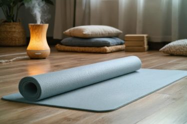 A peaceful home yoga space with a rolled-out mat on a warm wooden floor, surrounded by soft ambient lighting, meditation cushions, and an essential oil diffuser, creating a tranquil wellness sanctuary.