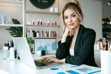 A female entrepreneur confidently planning finances in a chic beauty salon, surrounded by financial documents, a laptop with growth charts, and beauty products, symbolizing successful business strategy integration in the beauty industry.