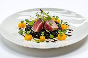 Beautifully plated gourmet dish showcasing a vivid color contrast with seared tuna, black rice, and bright green microgreens, illustrating the art of culinary presentation.