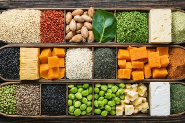 A colorful array of plant-based complete protein sources, featuring quinoa, buckwheat, tempeh, tofu, edamame, hemp seeds, chia seeds, and spirulina, arranged on a rustic wooden surface to represent a balanced and nutritional diet without meat.