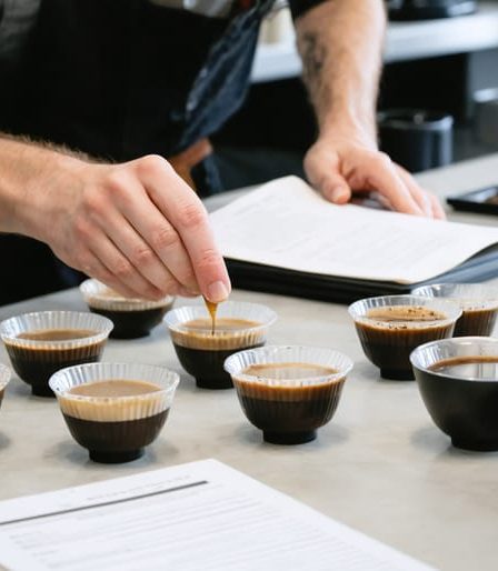 A professional Q Grader deeply focused on evaluating multiple coffee samples during a well-structured cupping session, surrounded by various cups and official scoring sheets.