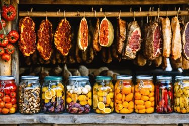 A collage showcasing various traditional food preservation methods, including sun-drying herbs and tomatoes on wooden racks, meats hanging in a traditional smokehouse, colorful jars of pickled vegetables, and salted cod drying by the sea.