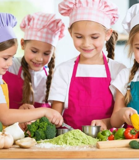 Energetic children wearing colorful aprons and chef hats enthusiastically participating in a hands-on cooking class, learning kitchen skills with fresh ingredients in a lively, bright kitchen setting.