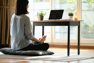 A person practicing mindfulness in a peaceful home office, sitting on a cushion in front of a desk with organized financial documents and calming elements like a plant and candle.