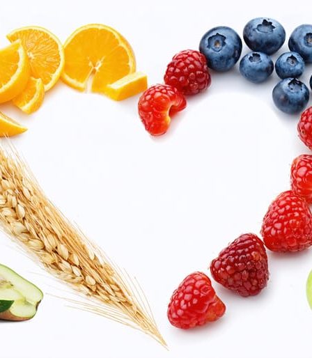 A heart-shaped arrangement featuring various plant-based, fiber-rich foods, highlighting the connection between fiber and overall wellness, including apples, berries, quinoa, oats, and green vegetables.