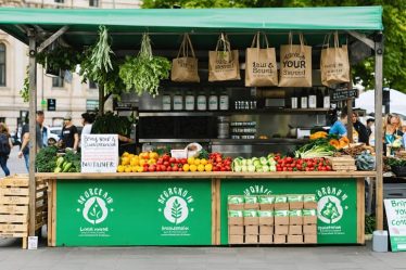 Street food vendor stall promoting eco-friendly practices with fresh produce and biodegradable packaging, highlighting community and sustainability in urban setting.