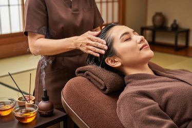 Therapist’s hands massaging a client’s scalp during a Japanese head spa, with warm oil bowls and a tranquil studio setting in the background.